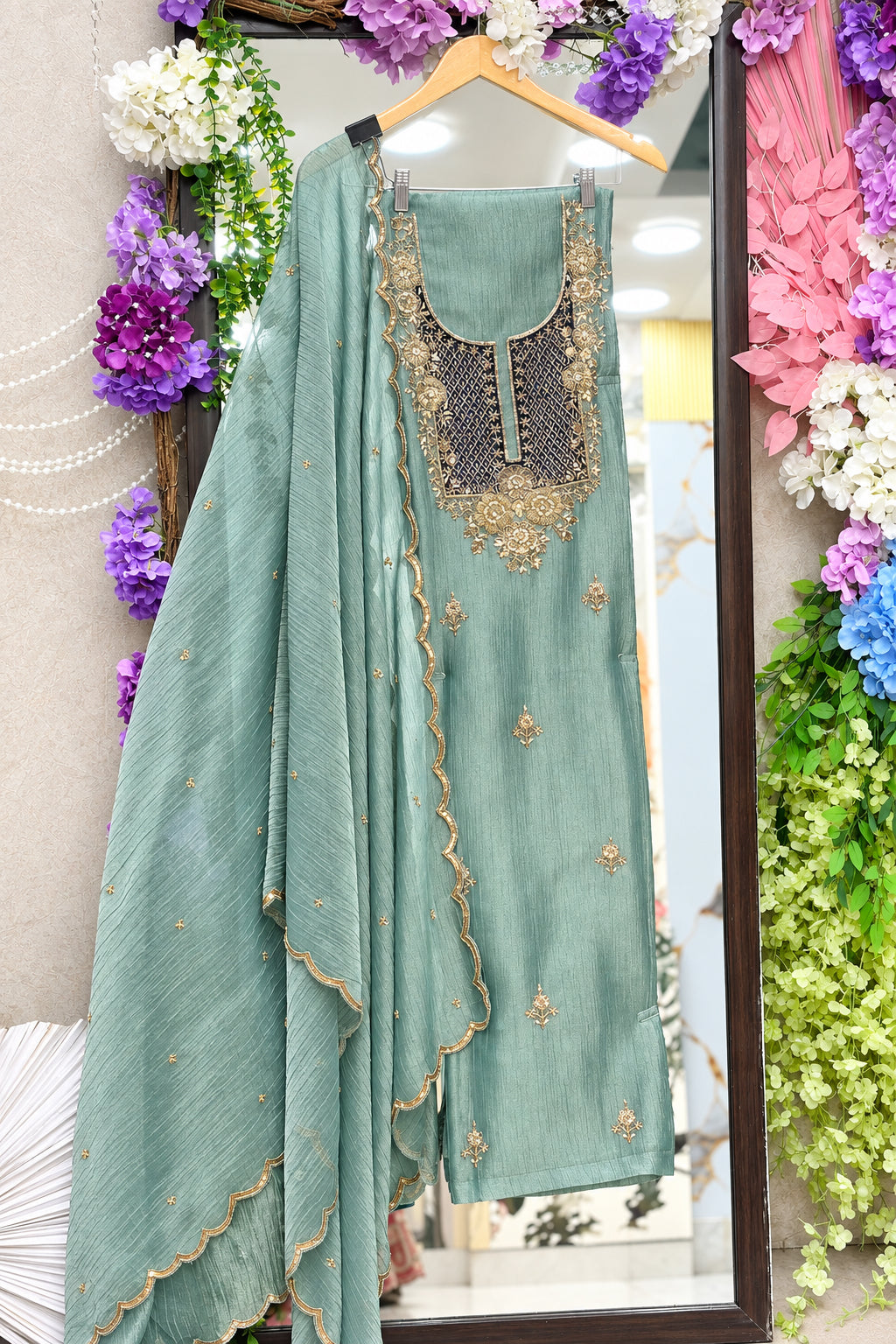 A sage green traditional Indian salwar suit set with a heavily embroidered neckline. The set includes a matching dupatta with scalloped edges and gold dabka embroidery.