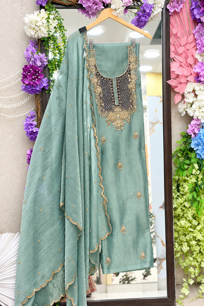 A sage green traditional Indian salwar suit set with a heavily embroidered neckline. The set includes a matching dupatta with scalloped edges and gold dabka embroidery.